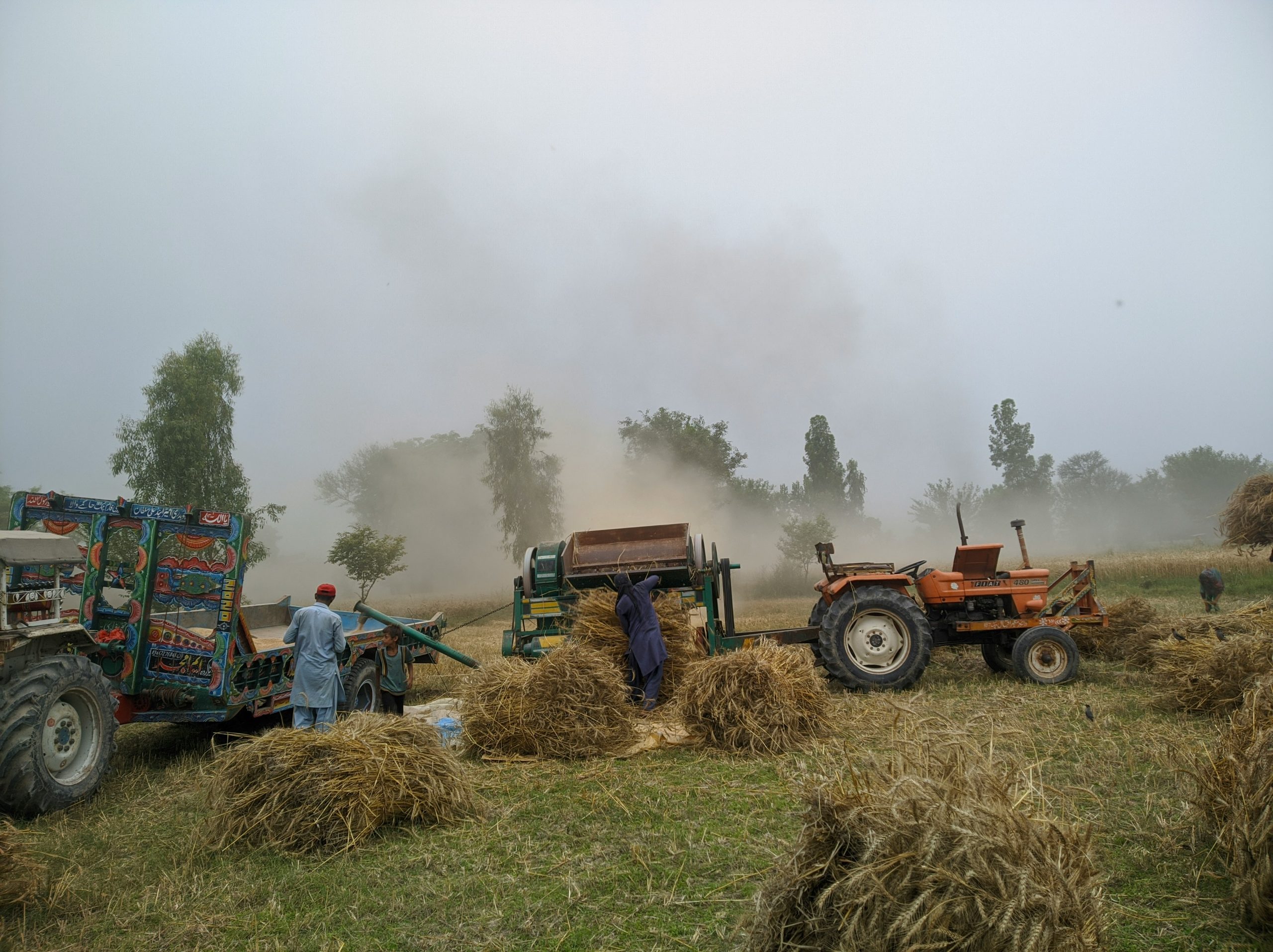 A field with tractors working in a dusty environment.